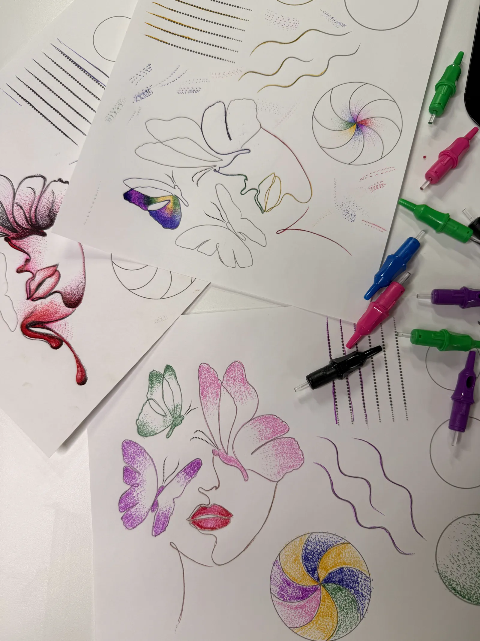 Practice sheets of stippled butterflies, faces, and swirls with colored cartridges